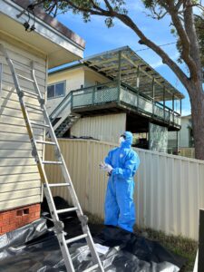 Asbestos Removal Sydney: a person in a blue suit and mask standing next to a ladder